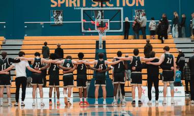 Basketball players stand together on a gymnasium court before a game.