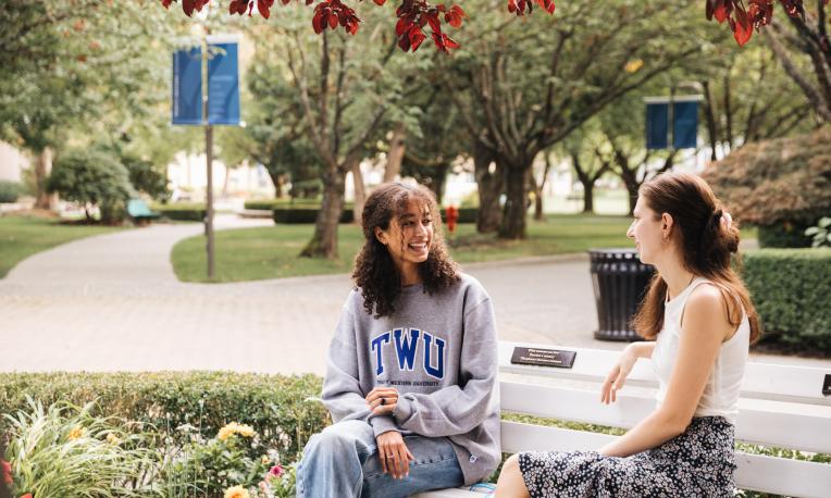 Two female students sitting on a bench talking at the TWU Langley campus.