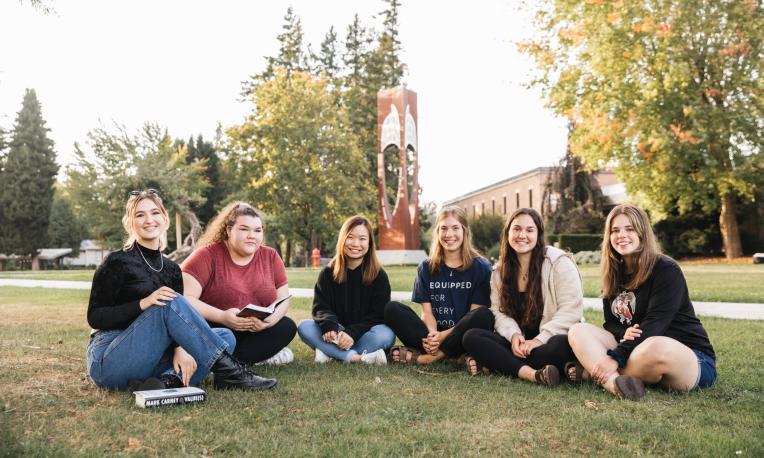 A group of female students sitting on the grass smiling at the camera.