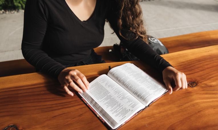 A female student sitting at a table reading the Bible