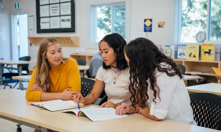 Three students looking at notebook on a desk