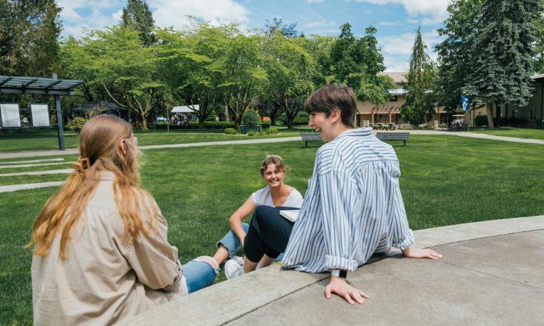 Three female students sitting on the steps of the outdoor chapel, smiling and talking
