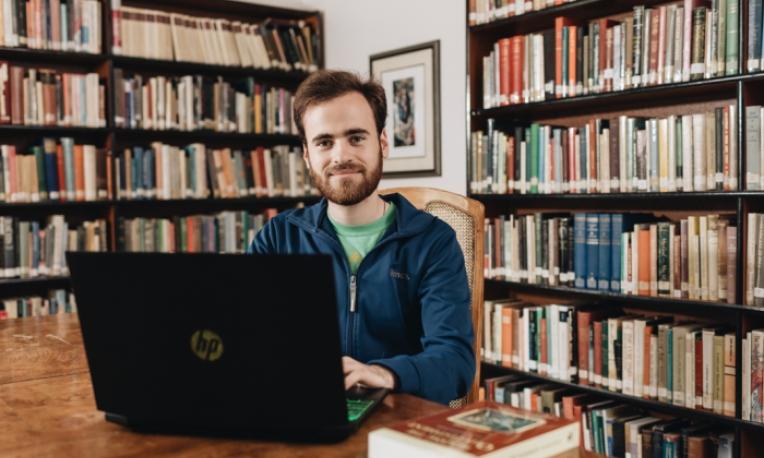 male student sitting in the library of the Catholic Pacific College smiling over his open laptop.