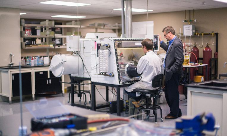 Research lab with student using a machine and professor instructing