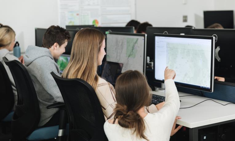 student pointing at screen with map in computer lab
