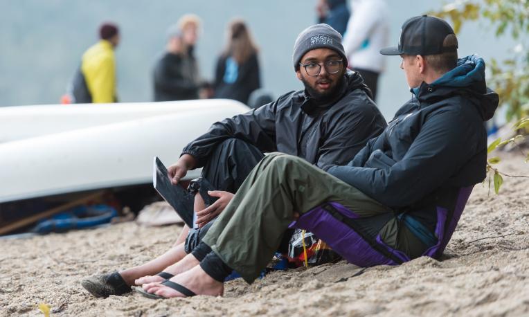 two people sitting on the ground and having a chat next to a boat