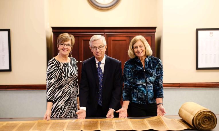 Three people stand with a Torah scroll.