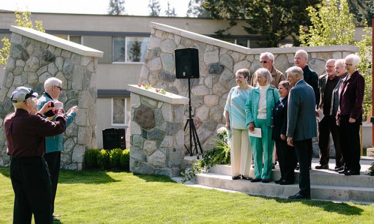 People taking pictures of a group of people standing on the steps of the outdoor chapel.
