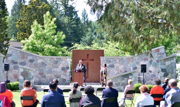A man stands on the outdoor chapel stage and addresses a crowd.