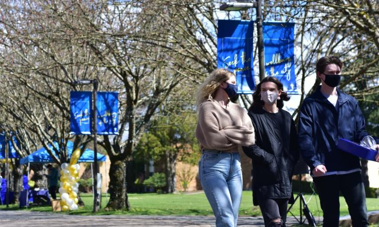 Three students wearing masks walk along the campus walkway.
