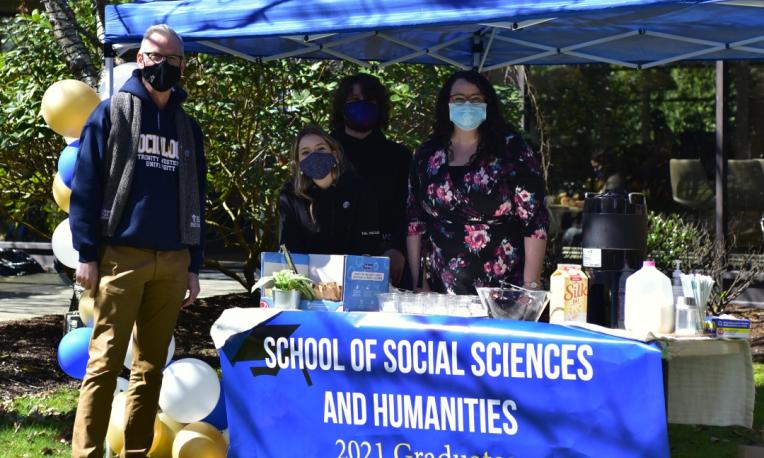 People pose in front of the booth of the School of Social Sciences and Humanities.