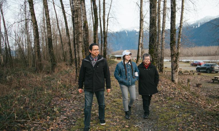 Three people walk along the path in a forest
