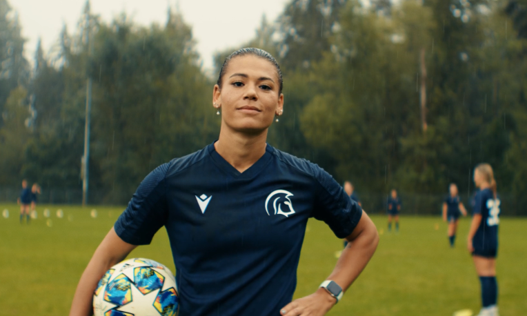 Aliya standing in a field in the rain holding a soccer ball