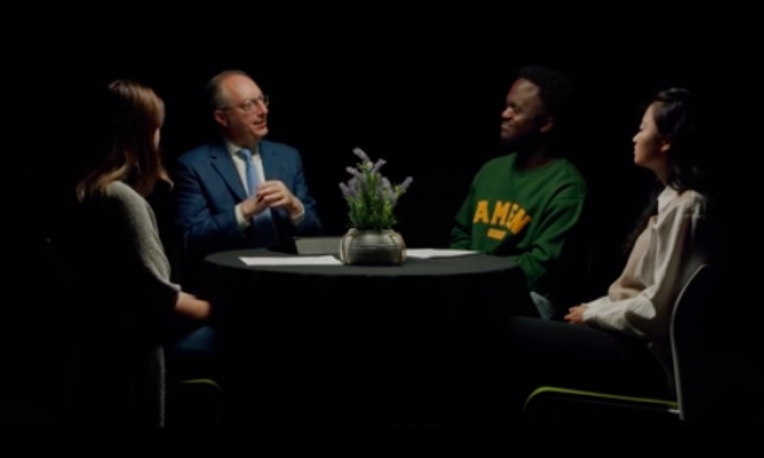 TWU president sitting at a table with three other students with a black background