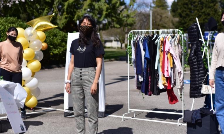 students standing on the pavement with masks on in front of a clothes rack