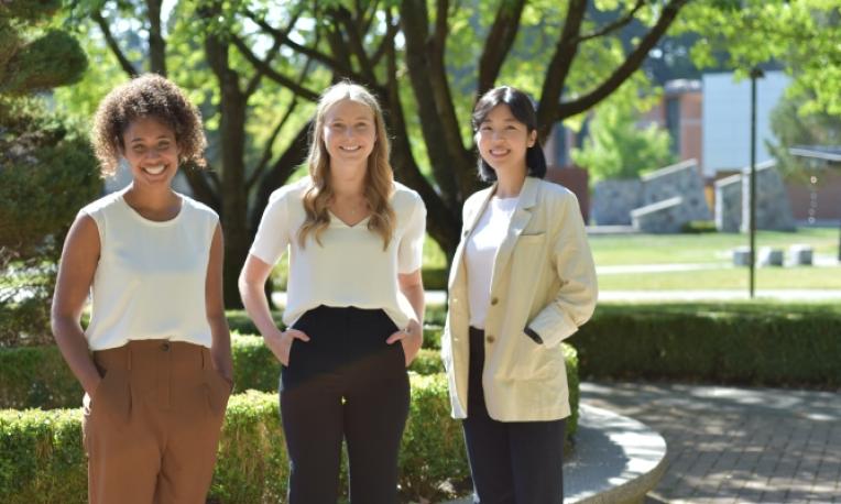 Three students posing with their hands in their pockets wearing light coloured shirts