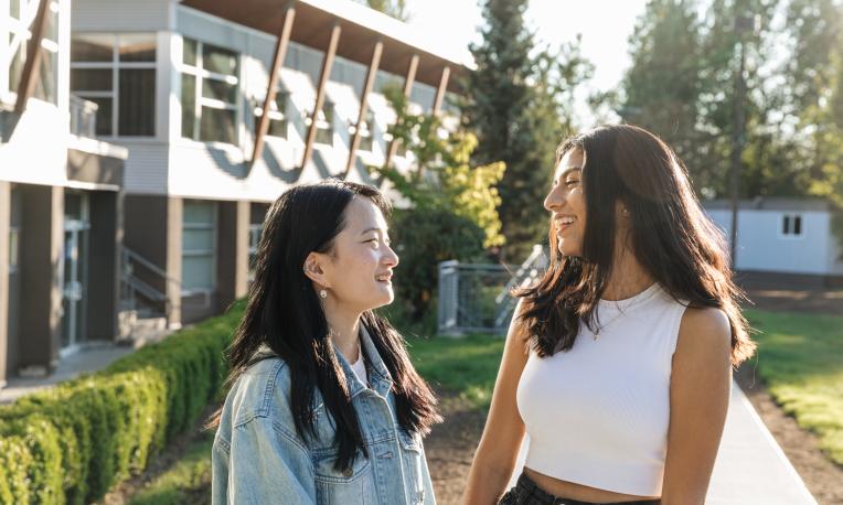 Two women smiling at each other outdoors near a modern building.