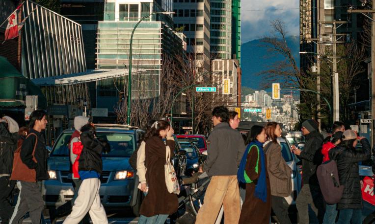 People crossing a busy city street, surrounded by tall buildings and cars.