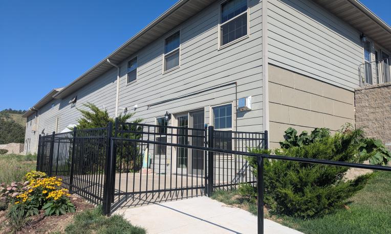 Modern building with beige siding, black fence, and garden in bright daylight.