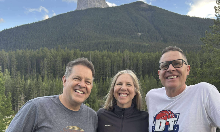 Three people smiling with a forest and mountain in the background.