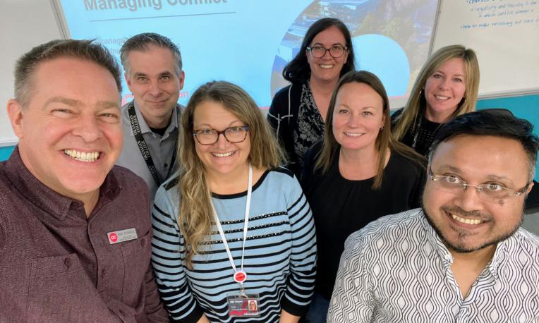 Smiling group in an office setting with a presentation slide in the background.