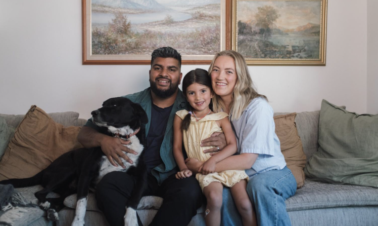 Family sitting on a couch with a black and white dog, smiling warmly.