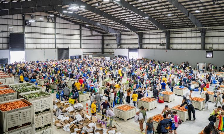 Crowded warehouse with volunteers sorting food donations.