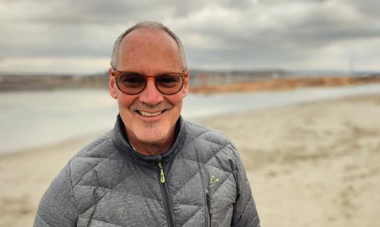 Smiling man in glasses on a cloudy beach.