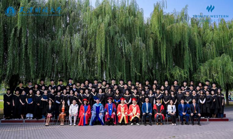 Graduation group photo under willow trees with diverse attire.