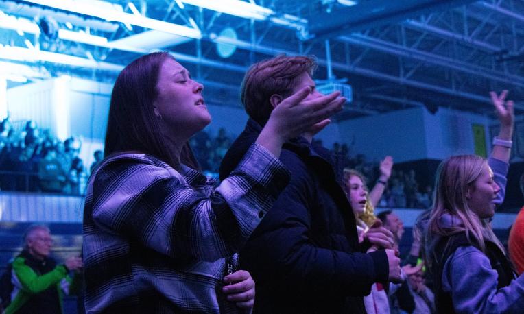 Concert audience under blue lighting, people with raised hands.