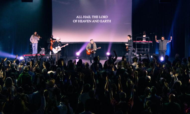 Concert scene with a band on stage and audience under colorful lights.