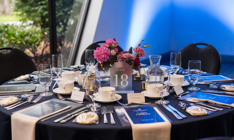 Elegant dining table with floral centerpiece, set for an event with blue lighting.