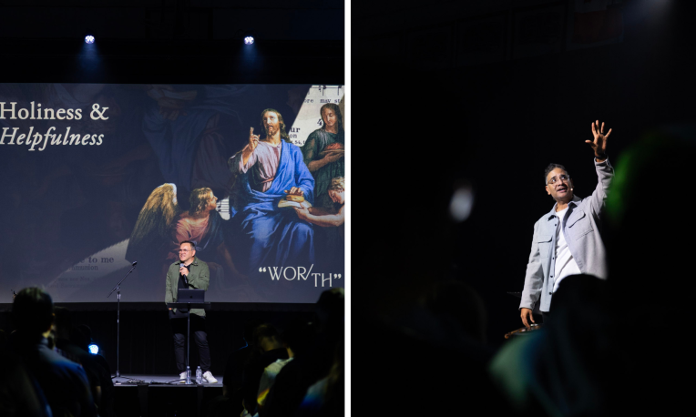 Man presenting on stage with large screen; another man gestures energetically under spotlight.