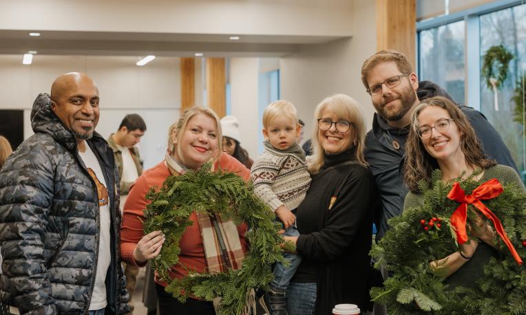 A family pose and smile at the camera, holding wreaths.