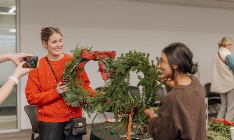 Two young women hold up wreaths and pose with smiles.