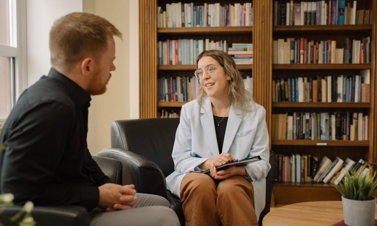 women and man sitting in chairs in front of a bookcase chatting