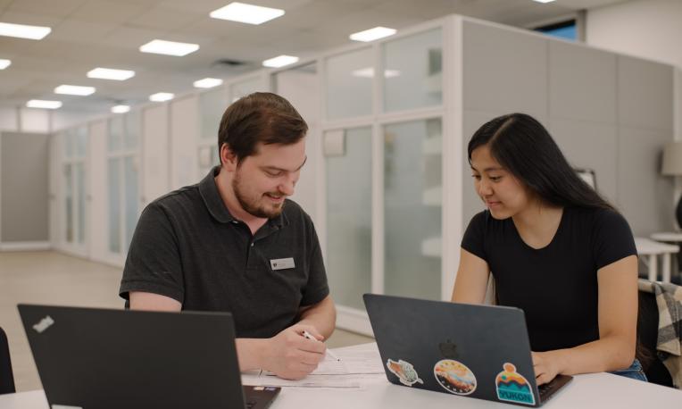 man sitting at a table helping student in the Learning Commons with laptops on a table