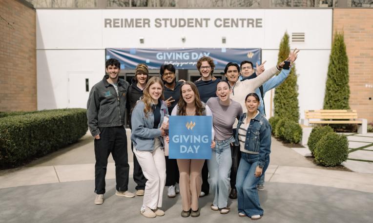 Students standing in front of Reimer Student Centre with Giving Day sign