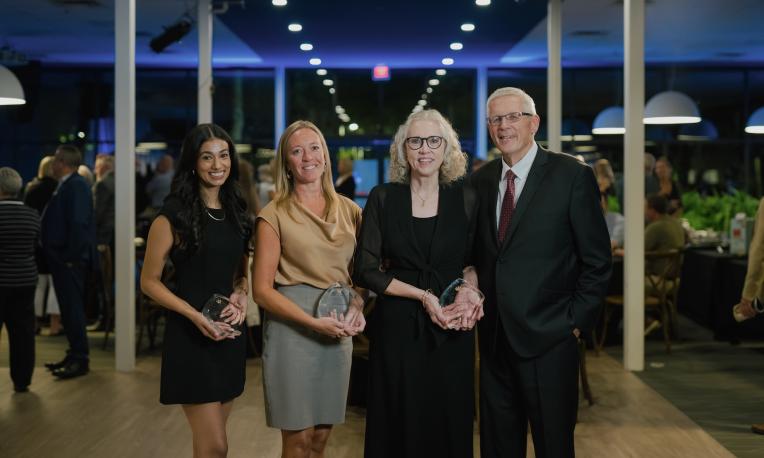 Four people pose together at an Alumni Awards event, with three holding glass awards.
