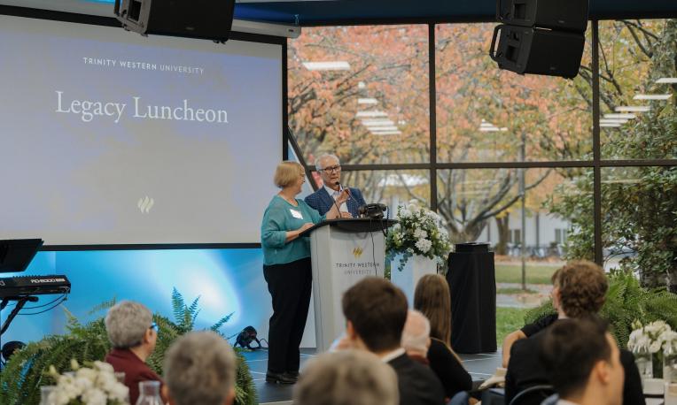 Paul and Janet Lermitte speaking at the podium during Trinity Western University’s Legacy Luncheon in Trinity Commons.