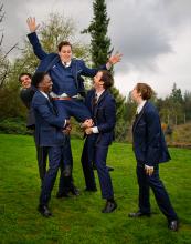 boys dressed in suits happily lifting one of their friends up on their shoulders