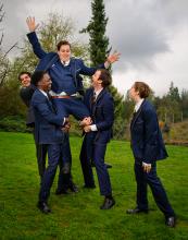boys dressed in suits happily lifting one of their friends up on their shoulders