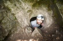 man crawling out of an opening within a rock