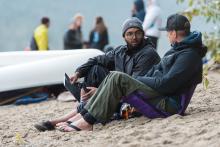 two people sitting on the ground and having a chat next to a boat
