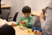 A young boy sitting at a table with a cup of liquid infront of him