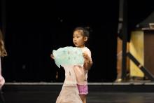A kid holding a pink and blue craft infront of a black wall