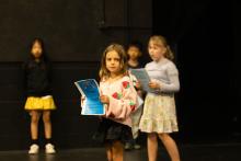Four kids holding pages of artwork in front of a black wall