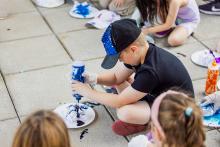 A boy sitting on a tiled floor squirting paint onto a paper plate