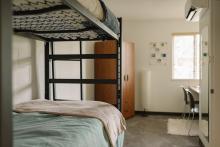 Furnished residence room with a bunk bed, desk, chair and window.