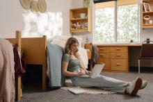 Student using a laptop while seated on the floor of a Robson Hall residence room.